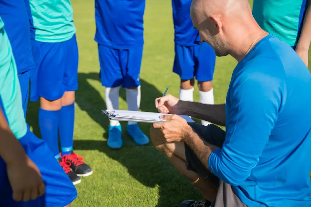 a man in blue shirt coaching a group of kids standing on a soccer field
