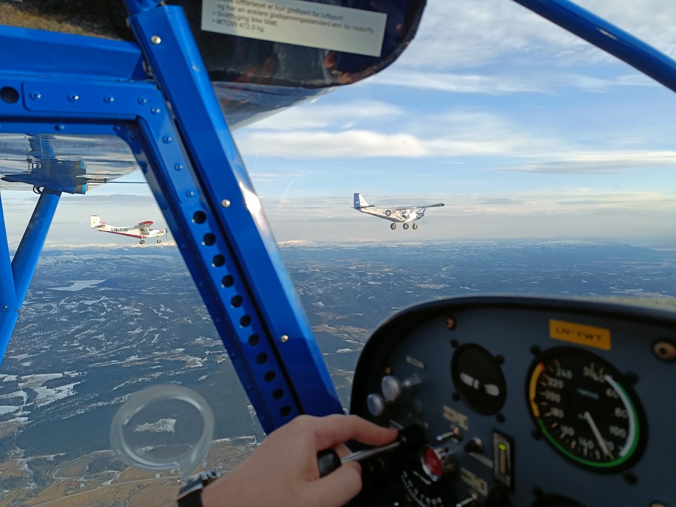 A person's hand on the control panel of a plane flying over a cityDescription automatically generated