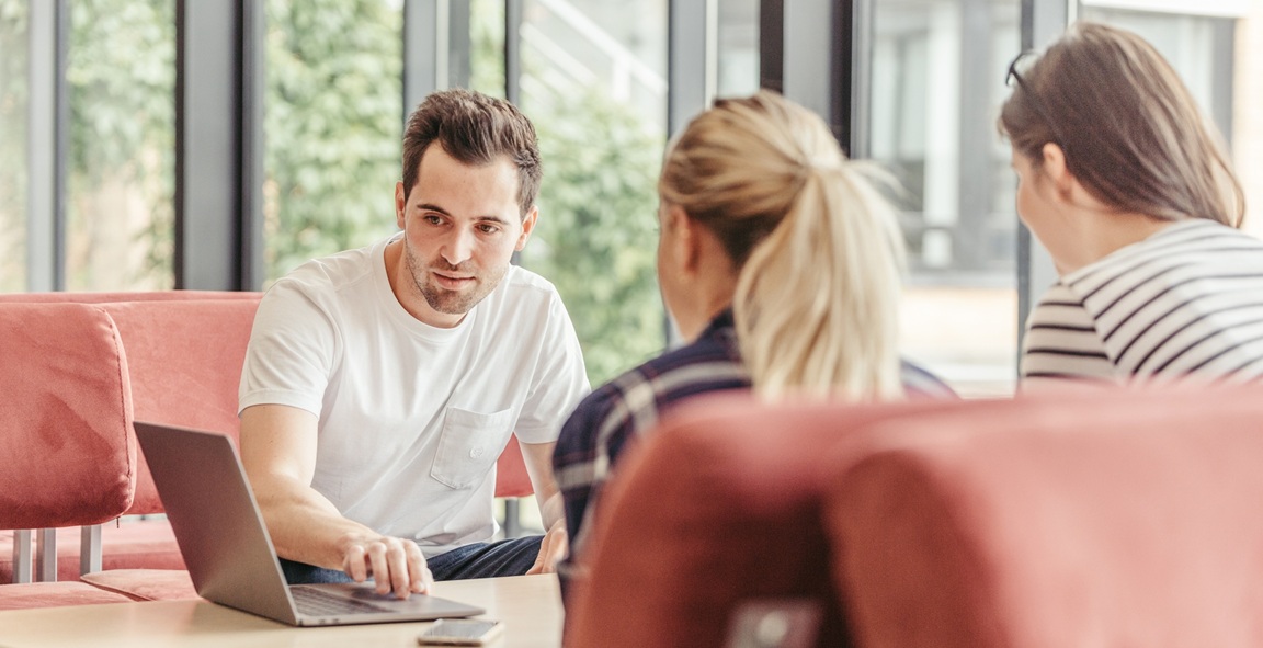 To menn og en kvinne sitter ved et bord og ser sammen på en laptop